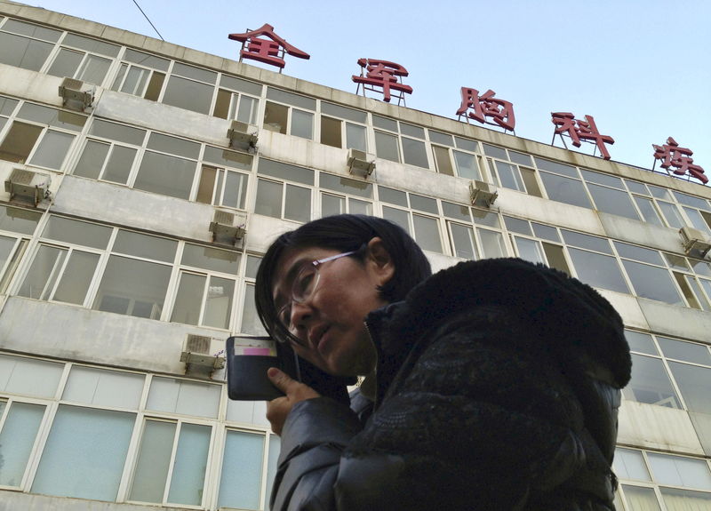 © Reuters. File photo of Wang Yu talking  on the phone in front of a hospital building where Cao is hospitalized at its intensive care unit in Beijing