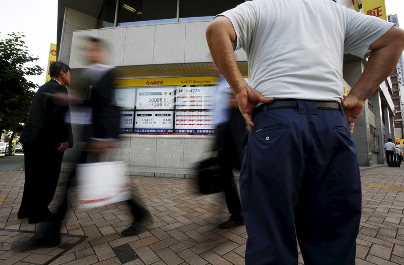 © Reuters. Passersby walk past an electronic stock quotation board outside a brokerage in Tokyo