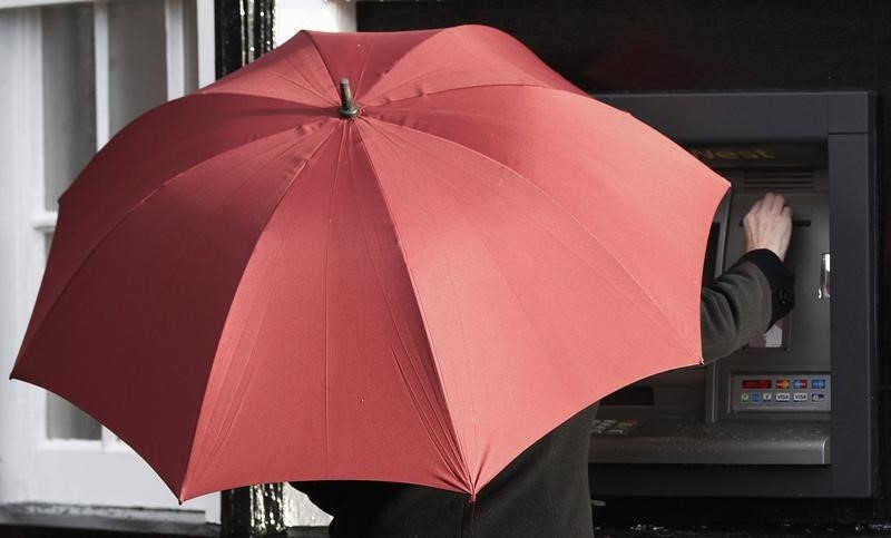 © Reuters. A woman shelters under an umbrella as she uses a cash machine in Port Sunlight, northern England