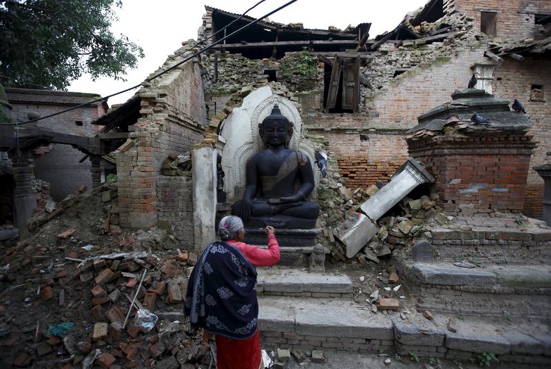© Reuters. A woman offers daily prayers at the statue of Lord Buddha that was damaged during the earthquake in Bhaktapur