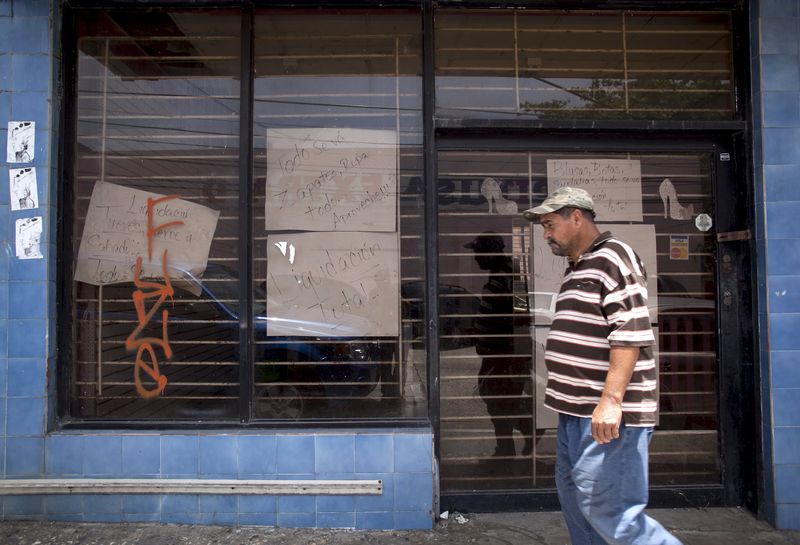 © Reuters. A man walks past a closed store with signs reading "Closing down sale" and "Everything goes, shoes, clothes, take advantage" in Arecibo, Puerto Rico