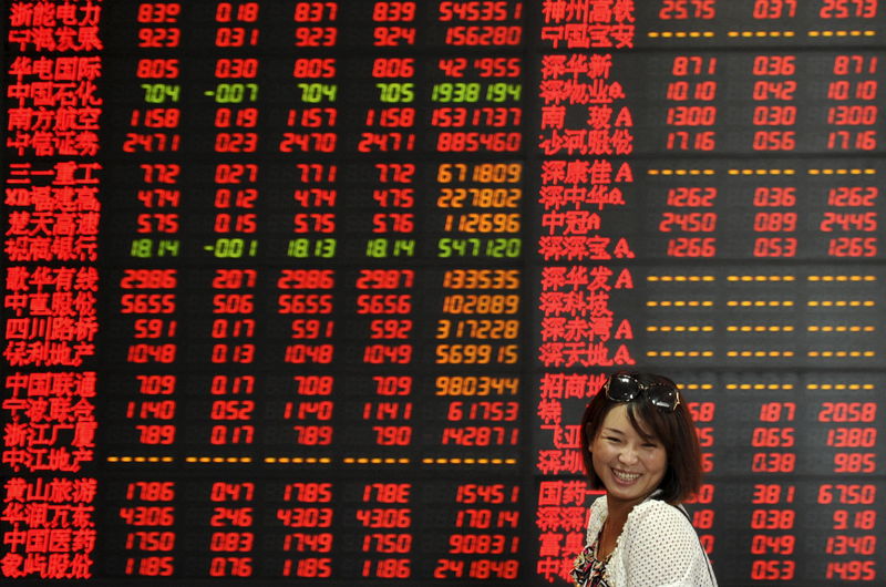 © Reuters. An investor smiles as she walks past an electronic board showing stock information at a brokerage house in Fuyang
