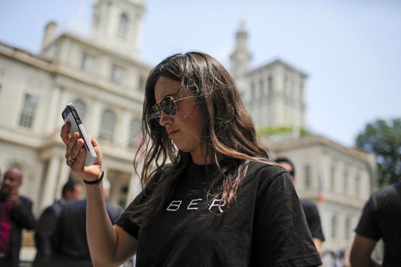 © Reuters. A woman wearing a Uber T-shirt checks her phone while Uber riders and driver-partners take part in a rally on the steps of New York City Hall against proposed legislation limiting for-hire vehicles in New York