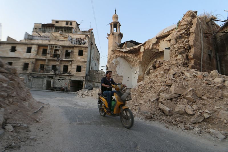 © Reuters. A man drives a motorcycle near damaged buildings in Old Aleppo's Kadi Askar area, Syria