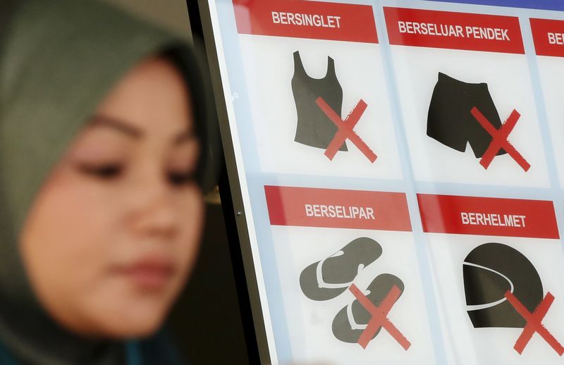 © Reuters. A woman walks past a sign with information about a dress code outside a government building in Kuala Lumpur