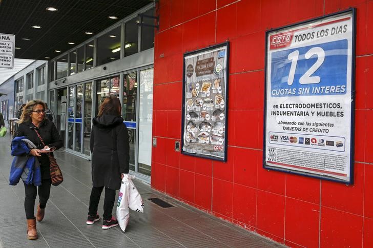 © Reuters. People look at posters offering a credit program allowing payment in 12 interest-free installments plasted on a supermarket wall in Buenos Aire