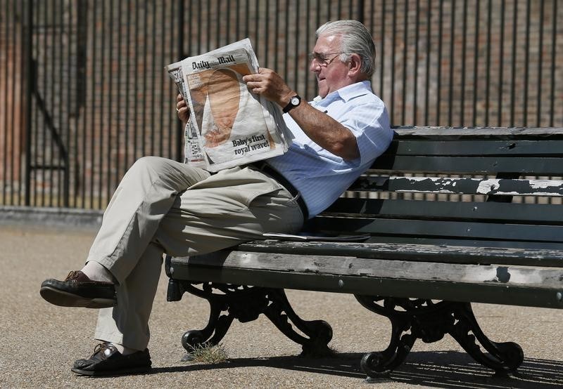 © Reuters. A man reads copies of Daily Mail newspaper featuring a picture of the newborn baby of Catherine, Duchess of Cambridge and Britain's Prince William, at Kensington Gardens in London