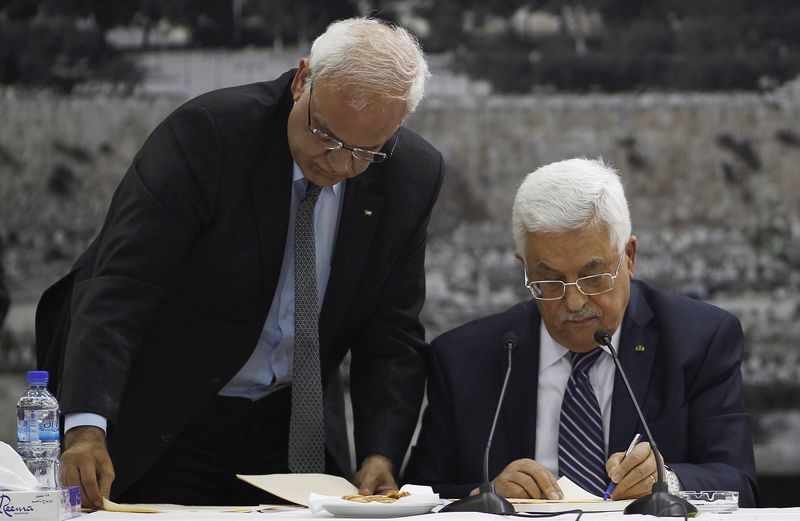 © Reuters. Erekat helps Abbas as he signs international conventions during a meeting with Palestinian leadership in the West Bank City of Ramallah