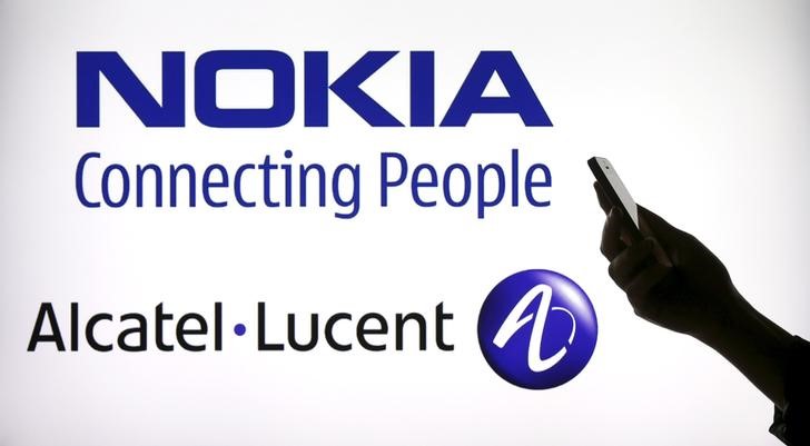 © Reuters. Photo illustration of a woman holding a smartphone in front of a screen displaying both Nokia and Alcatel Lucent logos in Paris