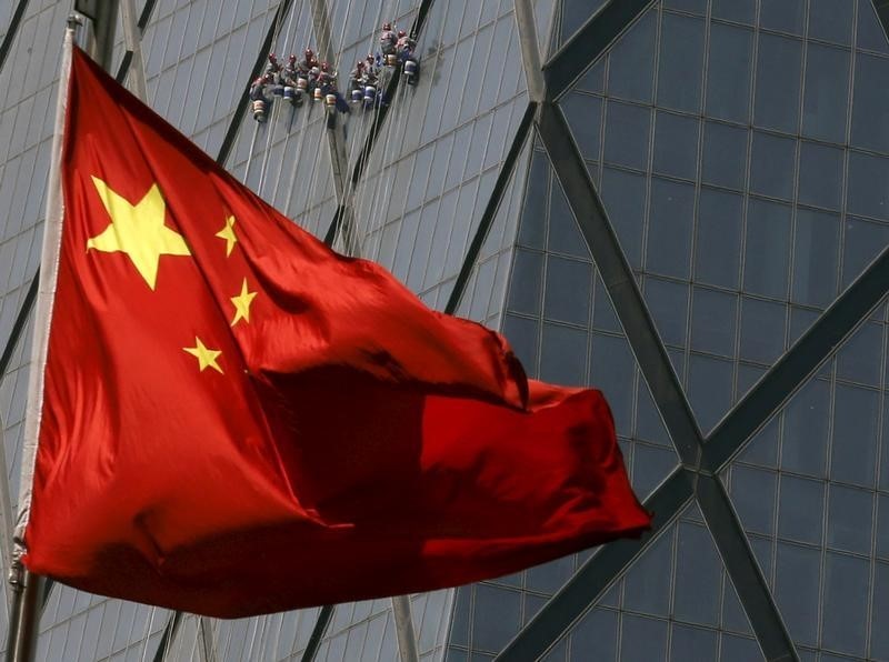 © Reuters. Workers cleaning windows of a building are seen behind China's national flag at a commercial district in Beijing