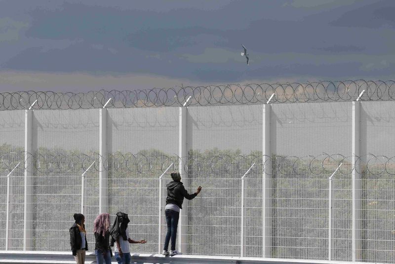 © Reuters. Migrants walk past the barbed wire fence on the main access route to the Ferry harbour Terminal in Calais, northern France