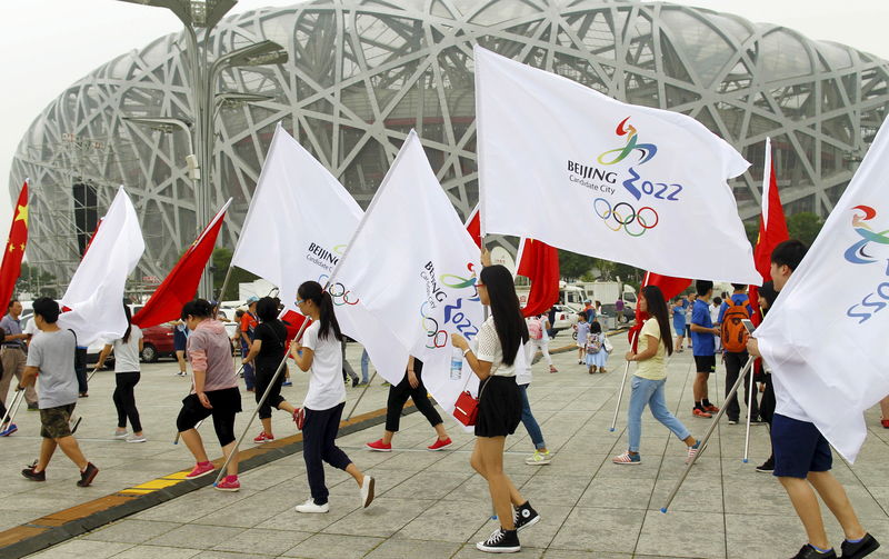 © Reuters. Participants holding Chinese national flags and Beijing 2022 Olympic flags walk past the Birds' Nest, also known as the National Stadium, to attend a rehearsal of a performance in Beijing