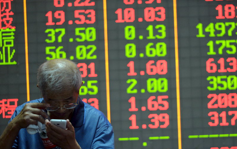 © Reuters. An investor checks on his mobile phone in front of an electronic board showing stock information at a brokerage house in Hangzhou