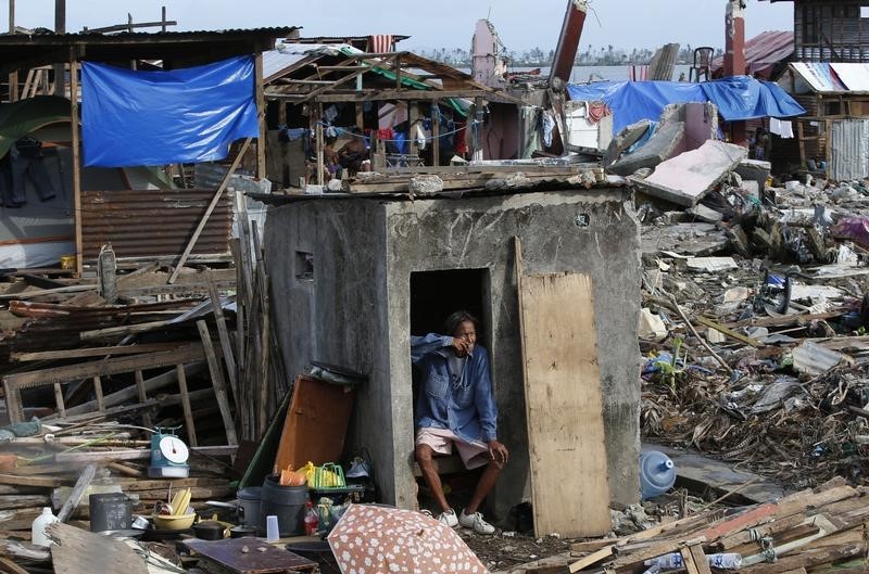 © Reuters. A typhoon survivor smokes a cigarette while resting by the entrance of his bathroom, the only part of his house still standing, in Tacloban city