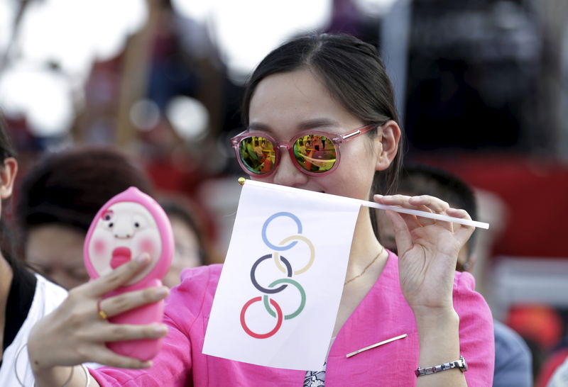 © Reuters. A local woman takes a selfie with an Olympics flag as she waits for IOC's announcement of the winner city for the 2022 winter Olympics bid in Chongli county of Zhangjiakou
