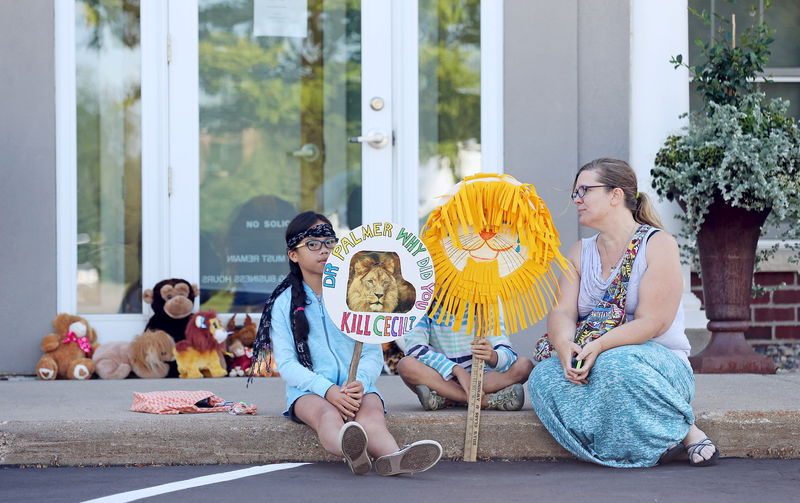 © Reuters. A family sits in front of the doorway of Bloomington's River Bluff Dental clinic in protest against the killing of a famous lion in Zimbabwe