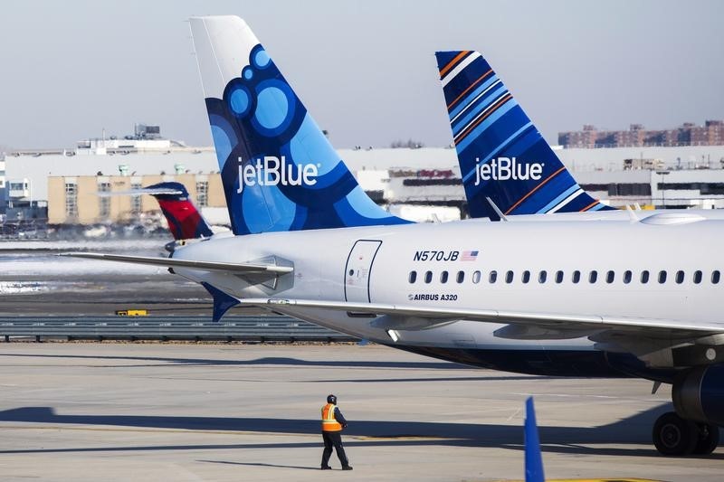 © Reuters. An airport worker leads JetBlue planes onto the tarmac of the John F. Kennedy International Airport in New York