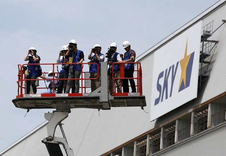 © Reuters. Photographers on a crane take pictures next to a logo of Skymark Airlines Inc at Haneda airport in Tokyo