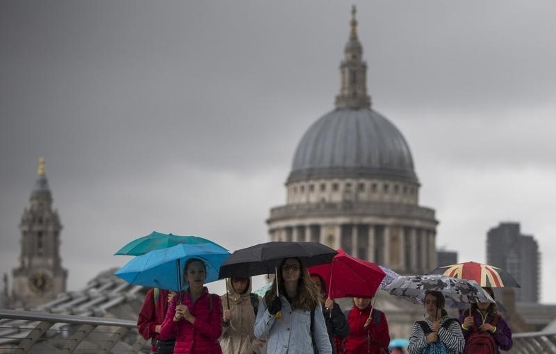 © Reuters. Tourists shelter under umbrellas as they cross the Millennium Bridge in front of St Paul's Cathedral on a rainy day in London