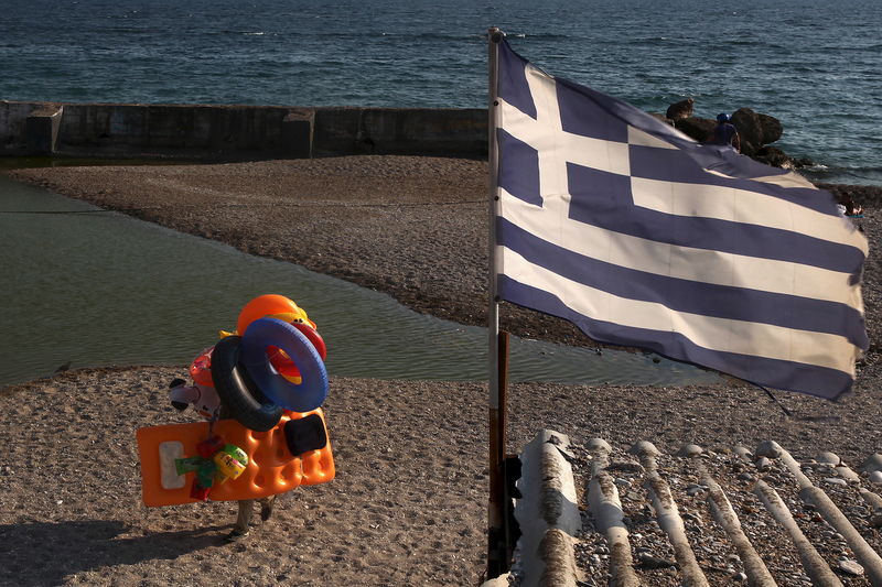 © Reuters. A beach vendor walks on the beach while a Greek flag flutters at a southern Athens suburb