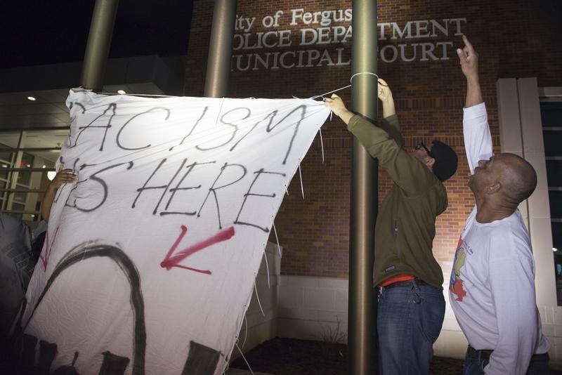 © Reuters. Protesters hang up a flag which reads, "Racism lives here", above a depiction of St. Louis, Missouri, outside the City of Ferguson Police Department and Municipal Court in Ferguson Missouri