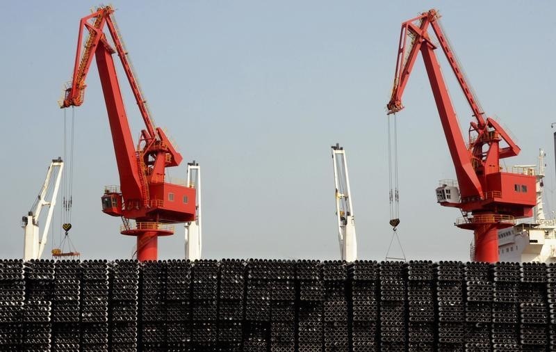 © Reuters. Piles of steel pipes to be exported are seen in front of cranes at a port in Lianyungang