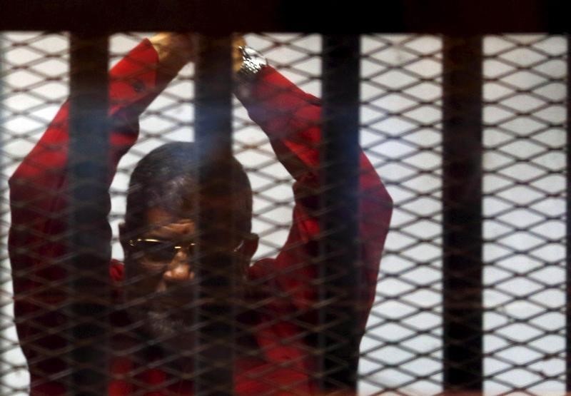 © Reuters. Deposed President Mohamed Mursi greets his lawyers and people from behind bars at a court wearing the red uniform of a prisoner sentenced to death, during his court appearance with Muslim Brotherhood members on the outskirts of Cairo, Egypt