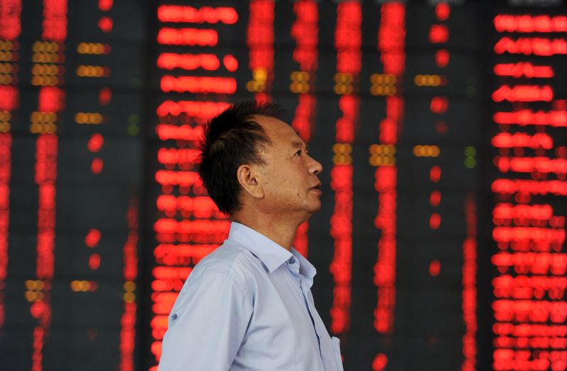 © Reuters. An investor stands in front of an electronic board showing stock information, filled with red figures indicating rising prices, at a brokerage house in Fuyang