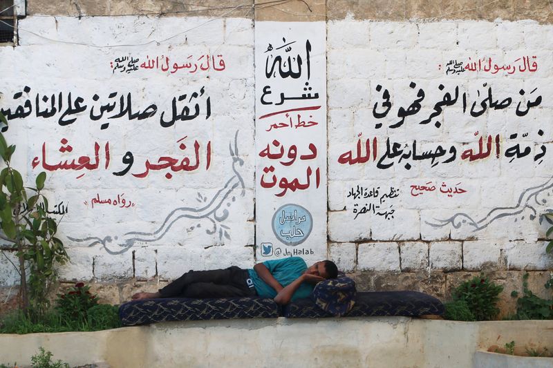 © Reuters. A man rests in front of a wall decorated with religious phrases written by members of al Qaeda's Nusra Front in Aleppo's Qadi Askar's neighborhood, Syria