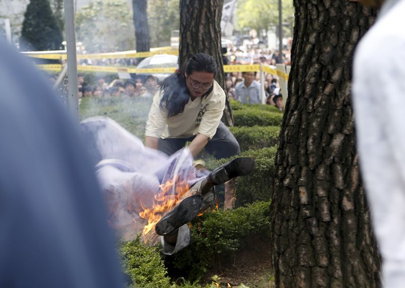 © Reuters. A man attempts to put out flames from another man who set himself on fire during a weekly anti-Japan rally in Seoul