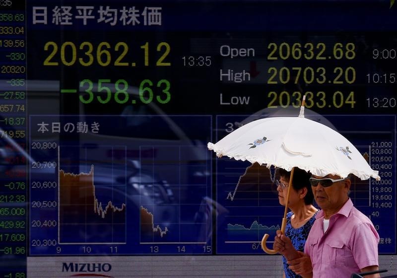 © Reuters. People walk past display showing Nikkei average in Tokyo