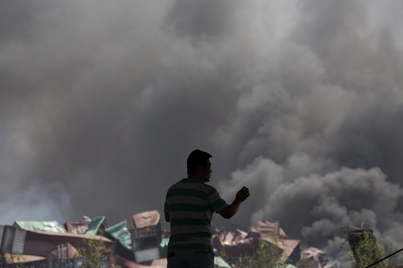 © Reuters. Homem olhando a fumação após explosão em Tianjin, na China