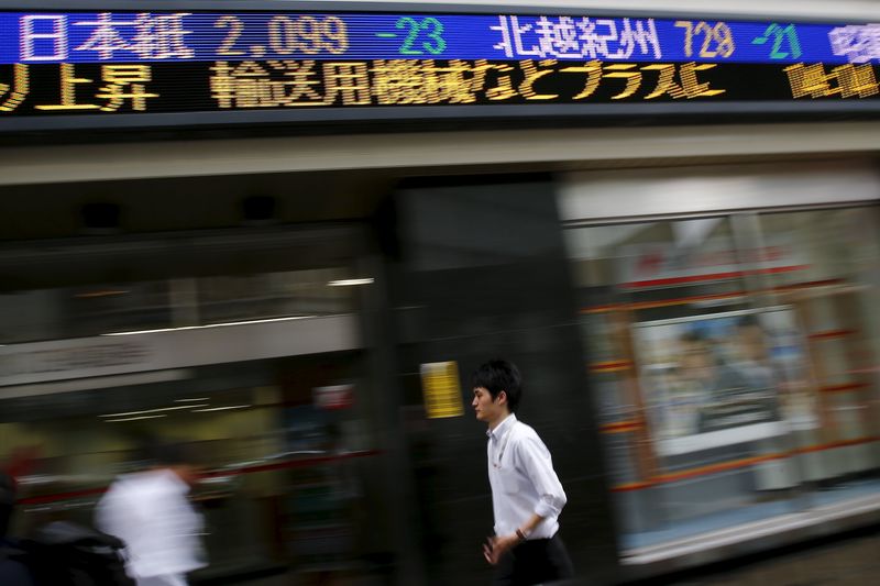 © Reuters. A man walks past display showing market indices in Tokyo