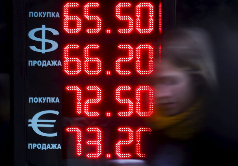 © Reuters. A woman walks past board, showing currency exchange rates of U.S. dollar and euro against rouble, in Moscow