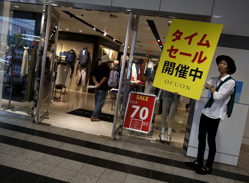 © Reuters. A man holds an advertisement board for a special offer for a limited time sale, outside a clothing retail store at a shopping district in Tokyo