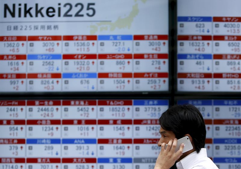 © Reuters. A pedestrian using his mobile phone walks past electronic boards showing the stock prices outside a brokerage in Tokyo