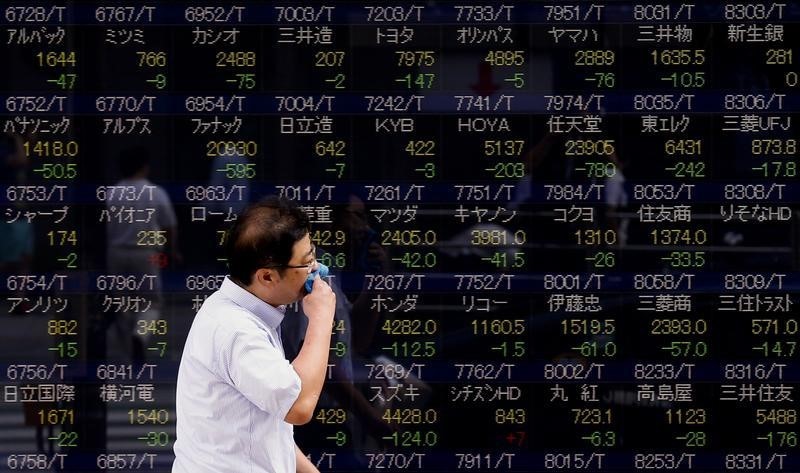 © Reuters. A man walks past display showing market indices in Tokyo