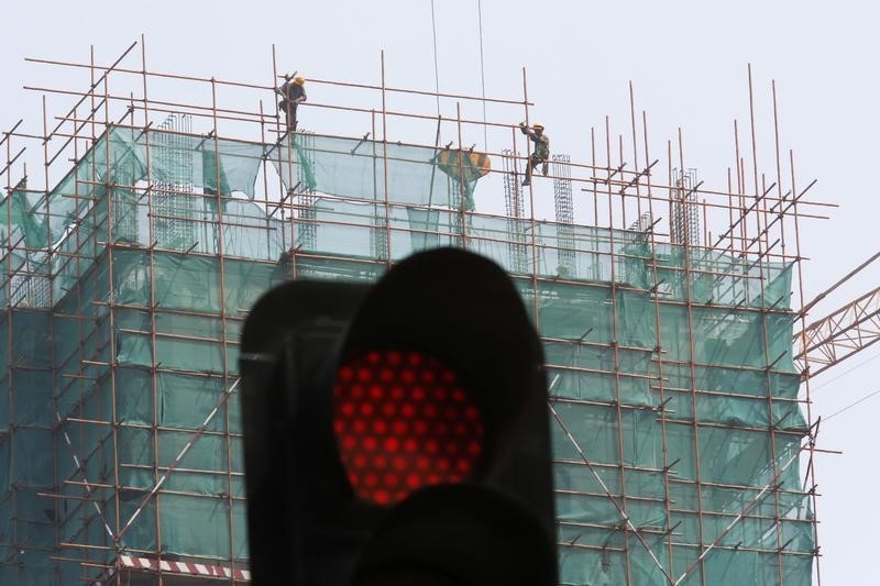 © Reuters. Construction workers are seen behind a traffic signal, at a site for a new business building, in Beijing