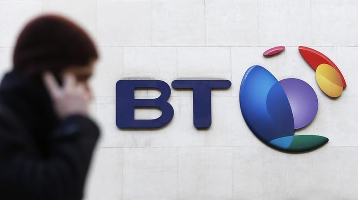 © Reuters. A man talks on his mobile telephone as he walks past a BT logo in London