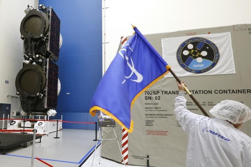 © Reuters. A man carries a flag with the Boeing logo past the world's first two all-electric propulsion 702SP satellites in the Boeing Satellite Development Center in El Segundo