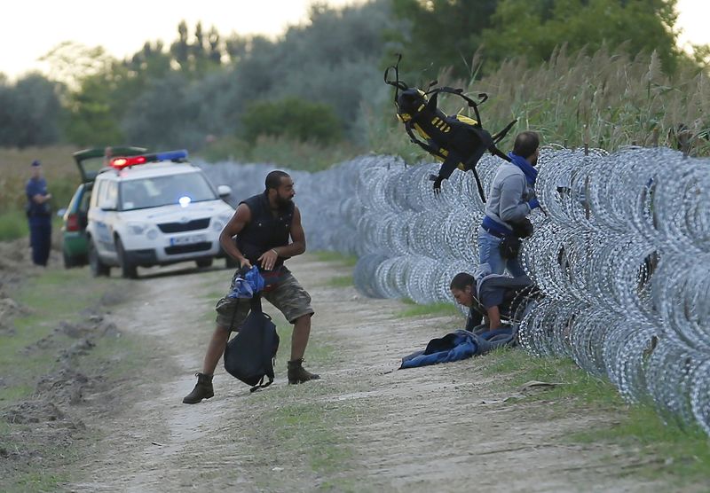 © Reuters. Migranti oltrepassano una barriera di filo spinato in Ungheria