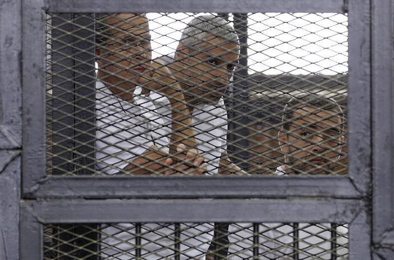 © Reuters. Al Jazeera journalists Greste, Fahmy and Mohamed stand behind bars at a court in Cairo