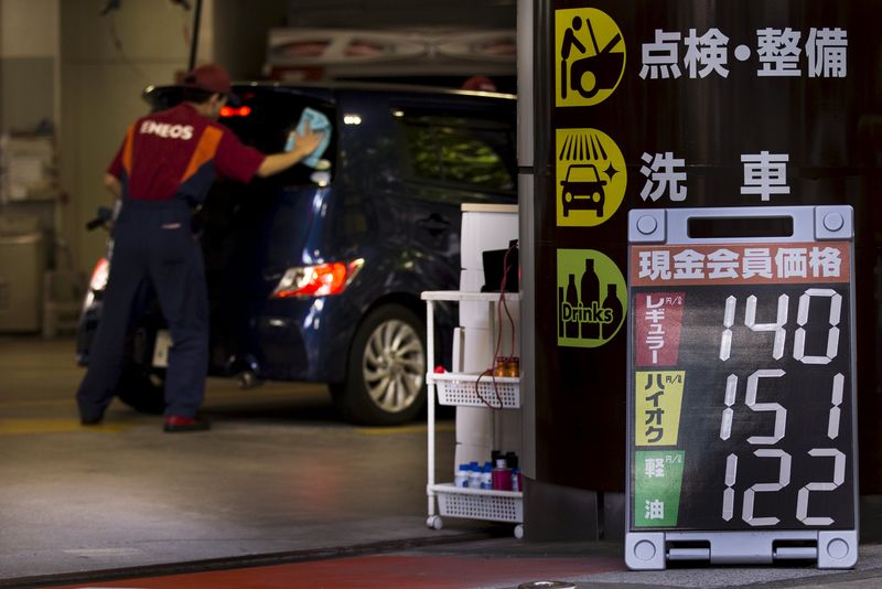 © Reuters. Attendant cleans the window of a car near a sign displaying the petrol station's current fuel prices in yen in Tokyo