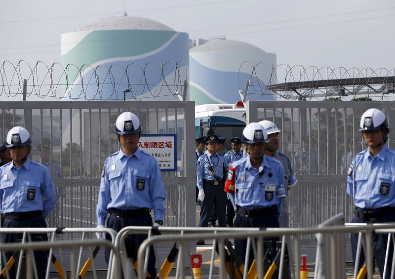 © Reuters. File photo of police officers and security personnel stand guard at an entrance of Kyushu Electric Power's Sendai nuclear power station in Satsumasendai