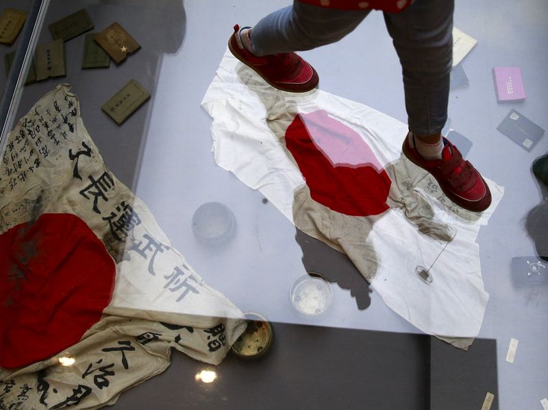 © Reuters. A visitor walks on a glass flooring above Japanese military flags seized by the Chinese PLA during World War Two, at the Museum of the War of Chinese People's Resistance Against Japanese Aggression, in Beijing