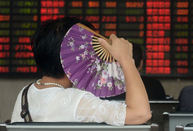 © Reuters. An investor holds a fan as she looks at stock information on an electronic board at a brokerage house in Shanghai