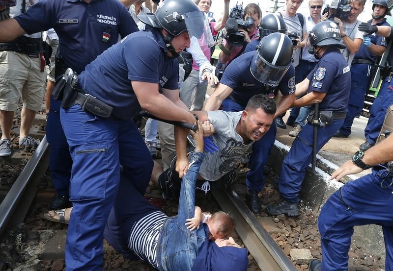 © Reuters. مهاجرون يرقدون على قضبان قطار بالمجر احتجاجا على نقلهم إلى مخيم