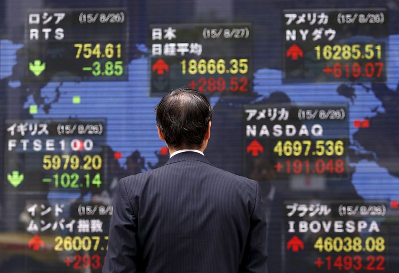 © Reuters. A pedestrian looks at an electronic board showing the stock market indices of various countries outside a brokerage in Tokyo