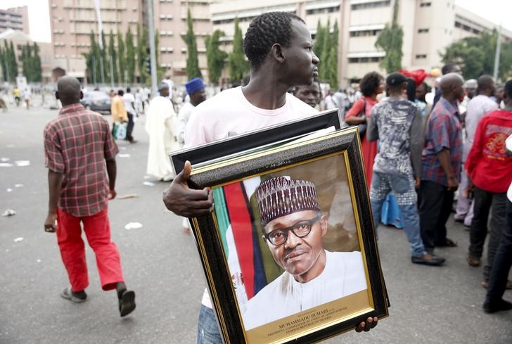 © Reuters. Man holds a framed portrait of Nigeria's President Muhammadu Buhari outside the venue of Buhari's inauguration in Abuja 