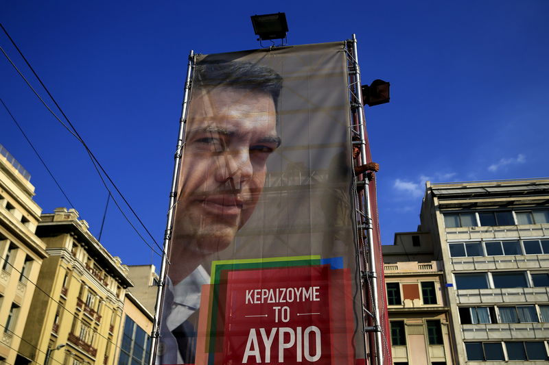 © Reuters. A worker hangs a banner with an image of former Greek prime minister and leader of leftist Syriza party Alexis Tsipras at the party's pre-election kiosk in Athens